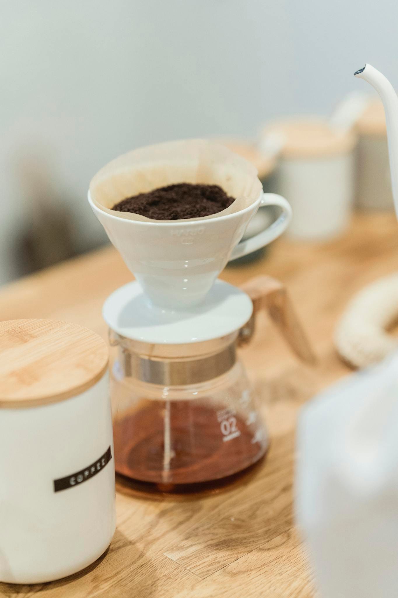 Elegant coffee brewing scene with ceramic dripper and glass pot on a wooden counter.
